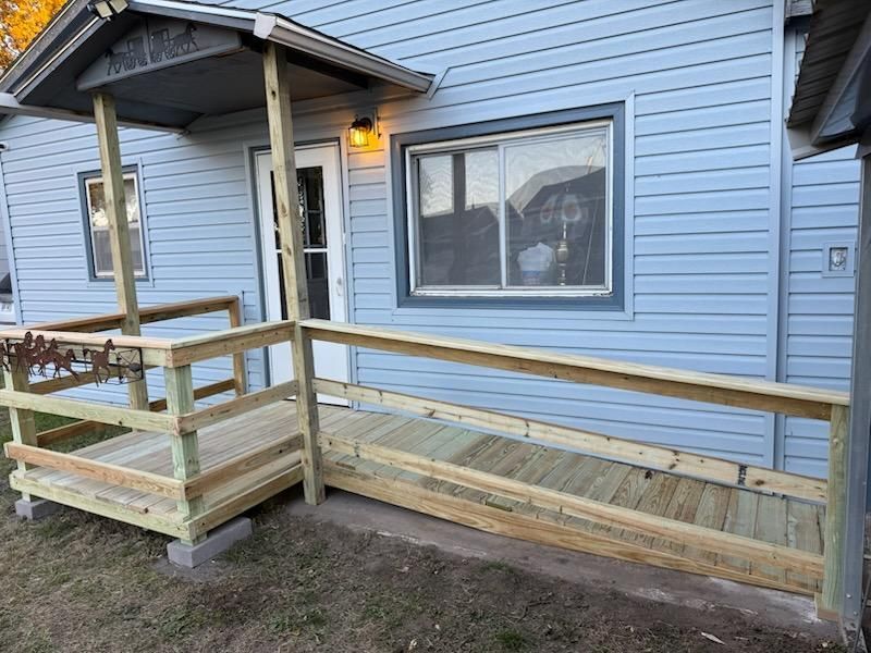 Wooden ramp with handrails leading to a light blue house entrance.