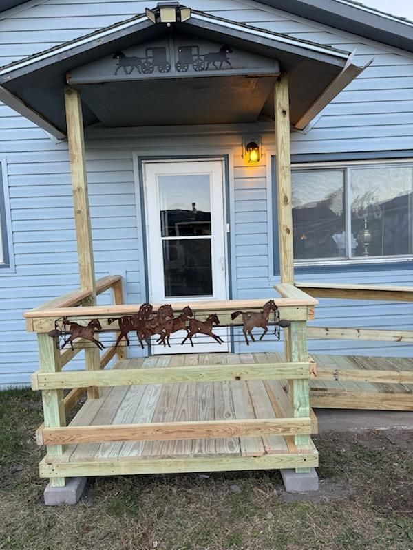 Wooden porch with a horse-themed metal railing and overhead cover in front of a blue house.