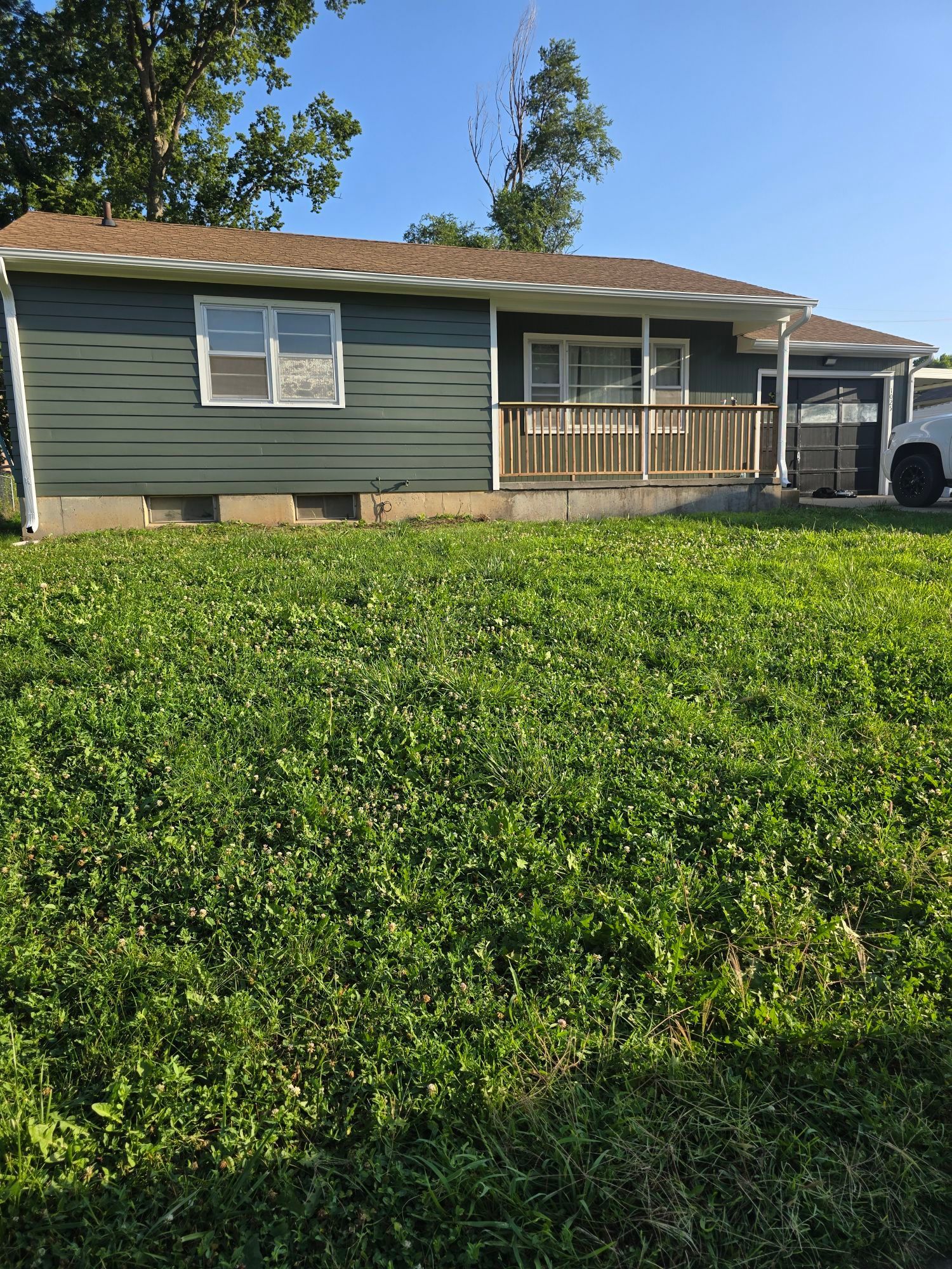 Green house with a wooden porch and green lawn under a bright blue sky.