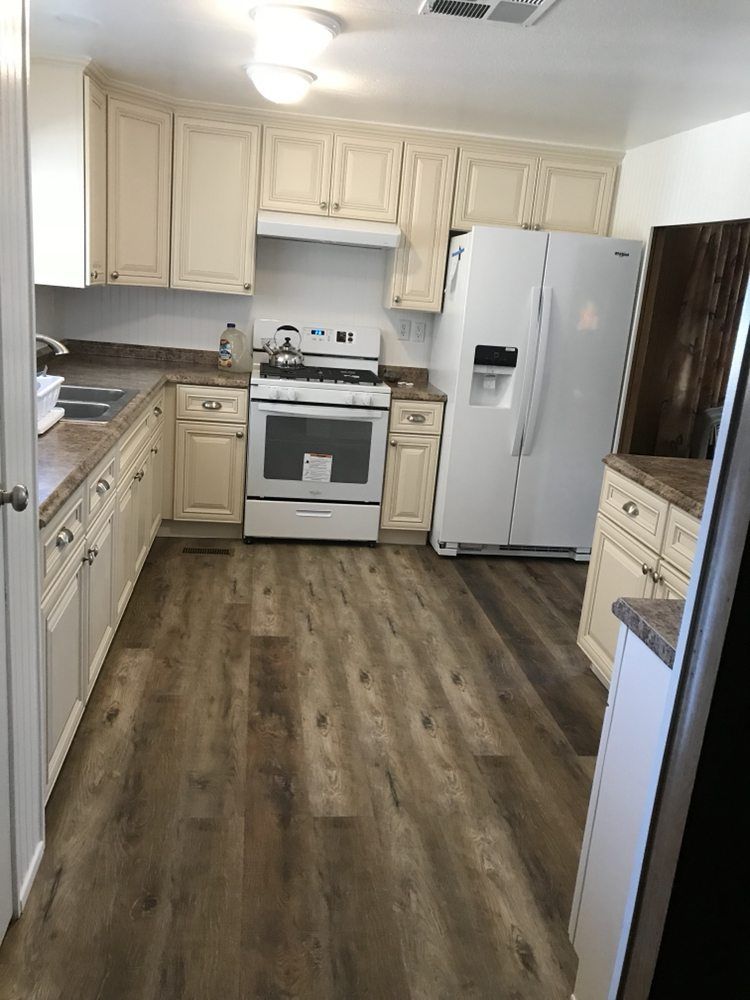 Kitchen with cream cabinets, white appliances, and wood-look flooring.
