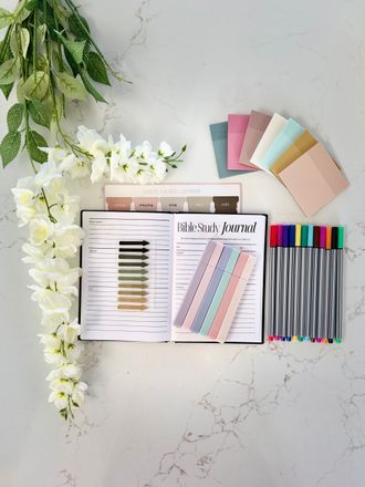 Planner and colorful stationery arranged on a marble desk with flowers and greenery.