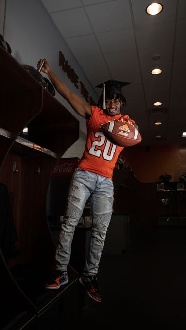 Football player in orange jersey posing indoors with a football and arm raised
