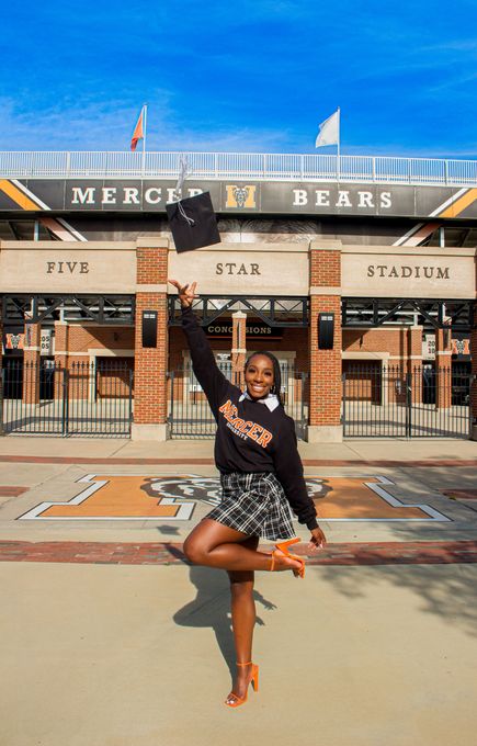 Person posing in front of a stadium entrance, wearing a black patterned outfit and orange heels.