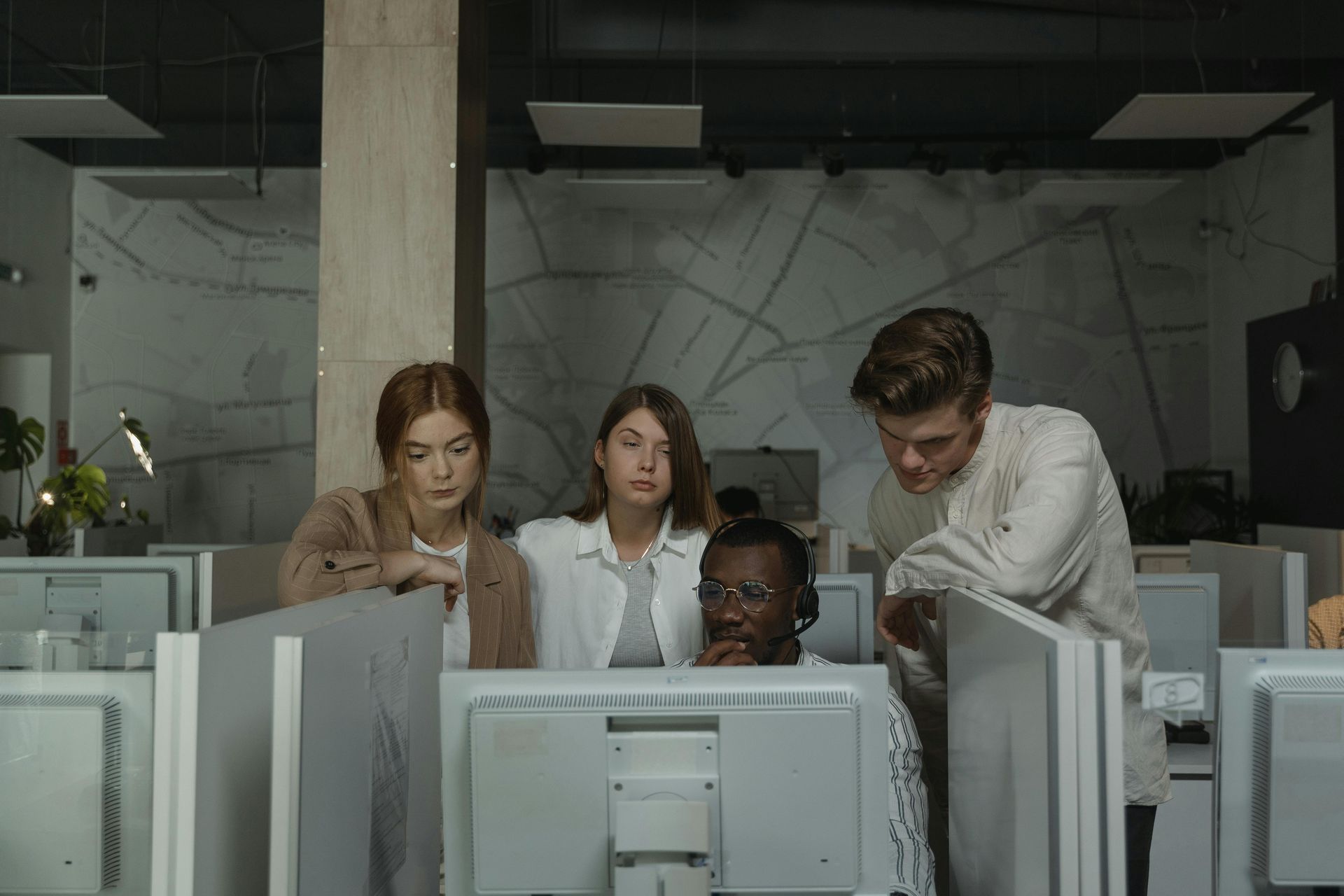 Four coworkers gathered around computer monitors in a dim office, reviewing something together