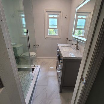 A bathroom with a sink , toilet , shower and mirror.