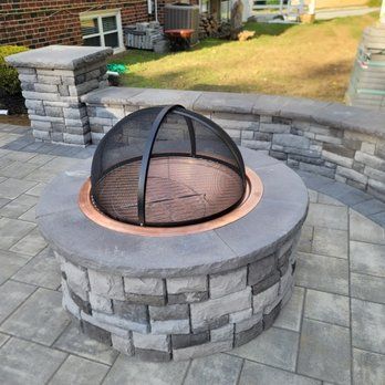 A fire pit is sitting on top of a brick patio next to a brick wall.