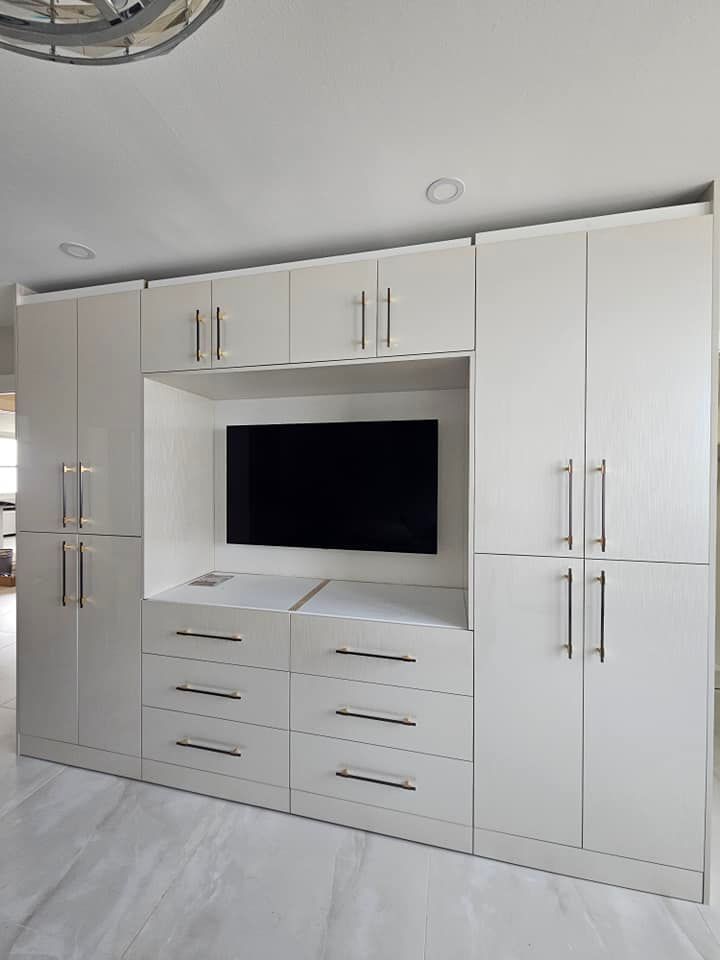 A wall of white cabinets with drawers and a flat screen tv