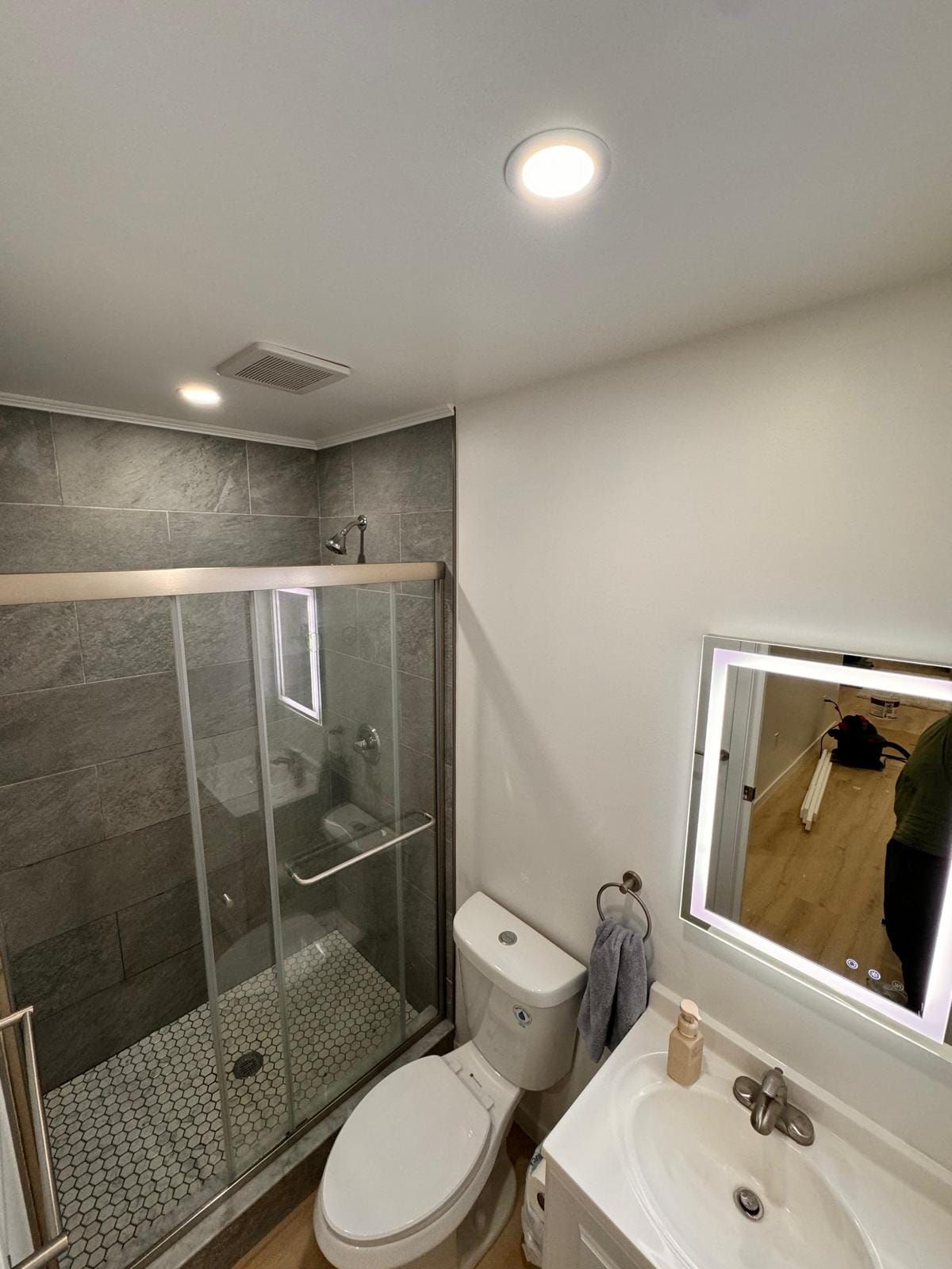A bathroom with a toilet , sink , shower and mirror.