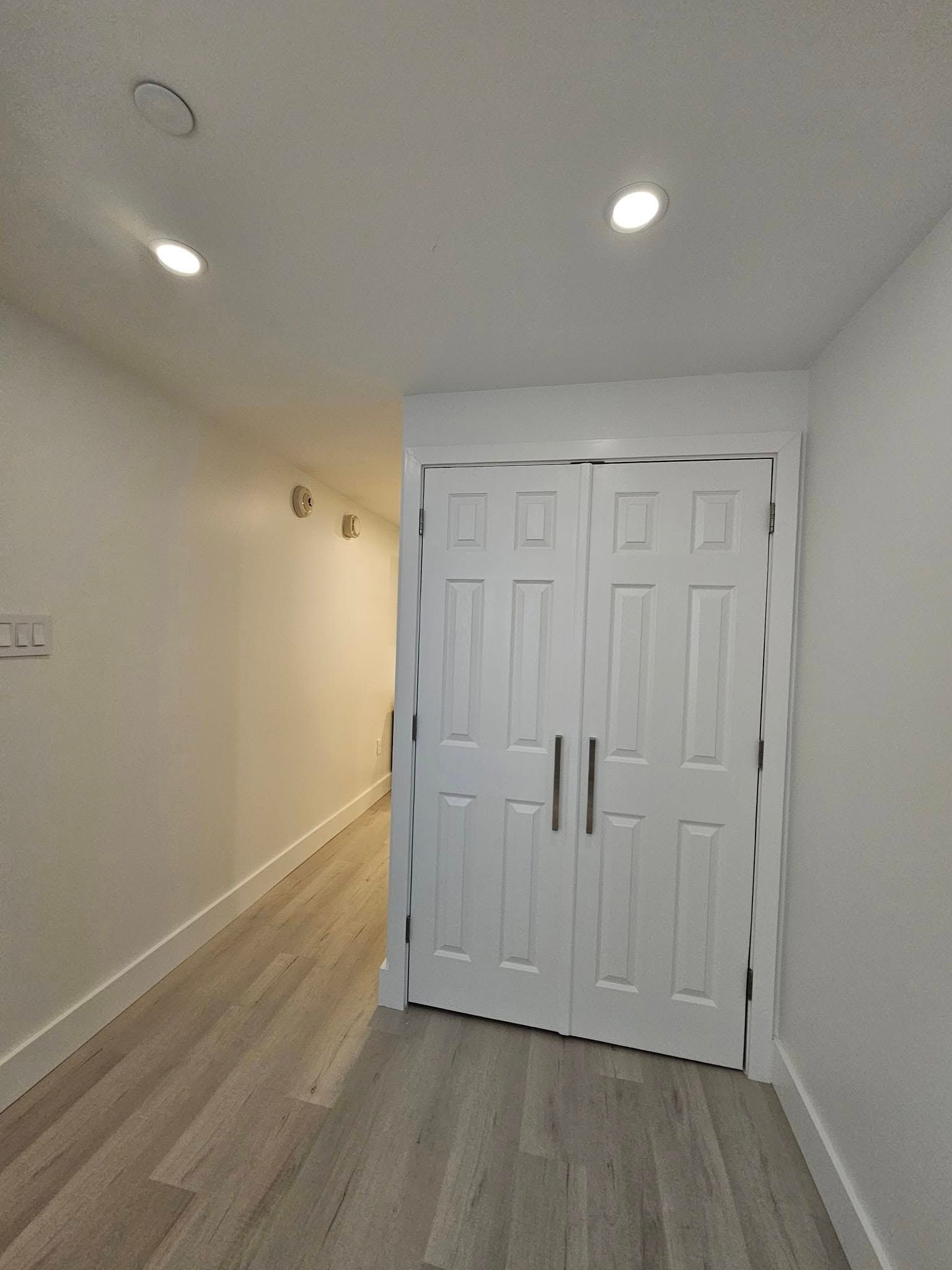 A hallway with hardwood floors and white doors leading to a closet.