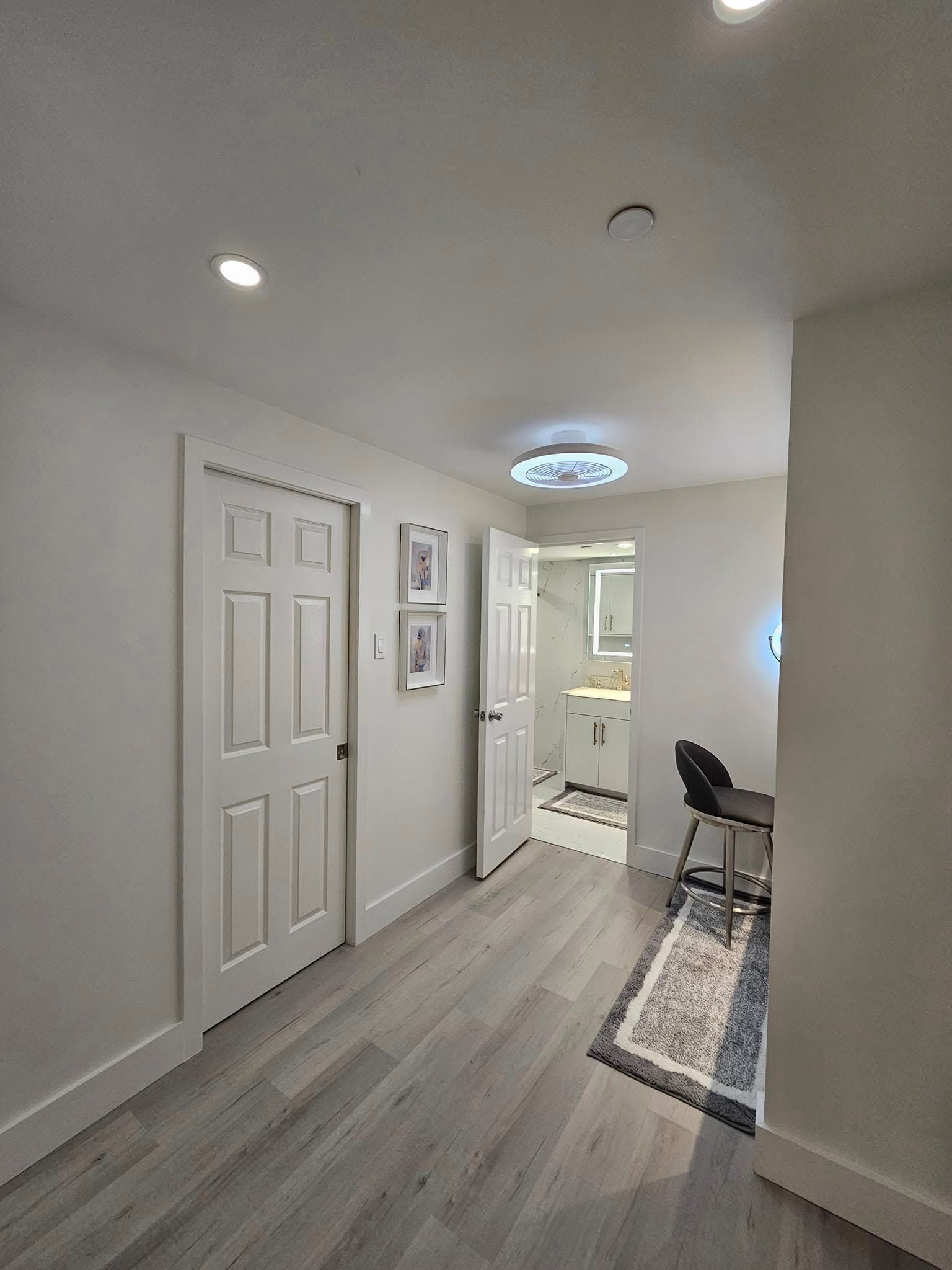 A hallway with hardwood floors and white walls leading to a bathroom.