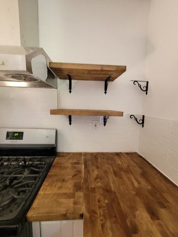 A kitchen with a wooden counter top , stove , and shelves.
