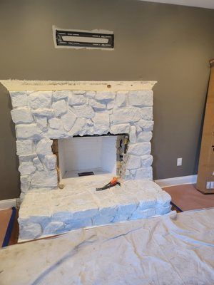 A white stone fireplace is being built in a living room.