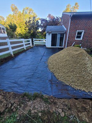 A driveway with a white fence and a pile of gravel in front of a brick house.
