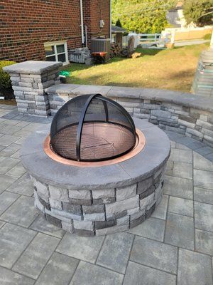 A fire pit is sitting on a patio next to a brick wall.