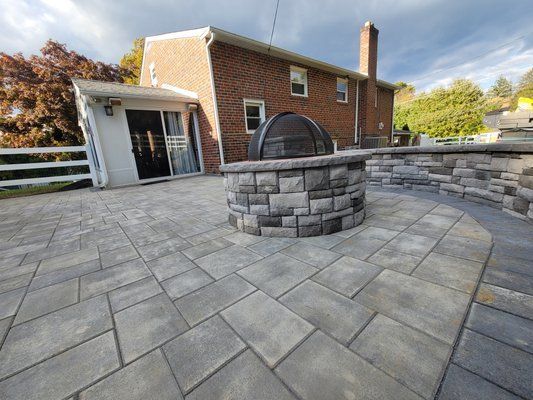 A fire pit is sitting on a patio in front of a brick house.