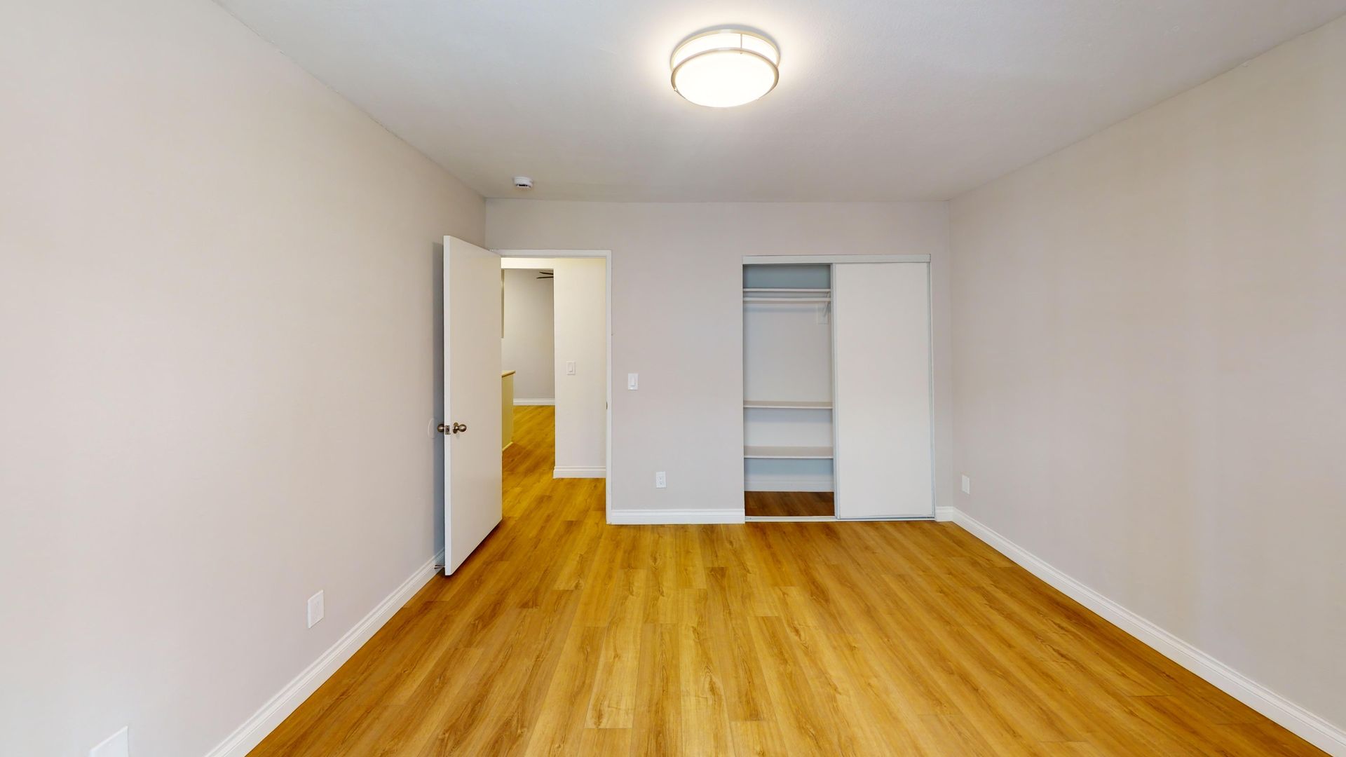 Empty room with wood floors, closet, and open door to hallway.