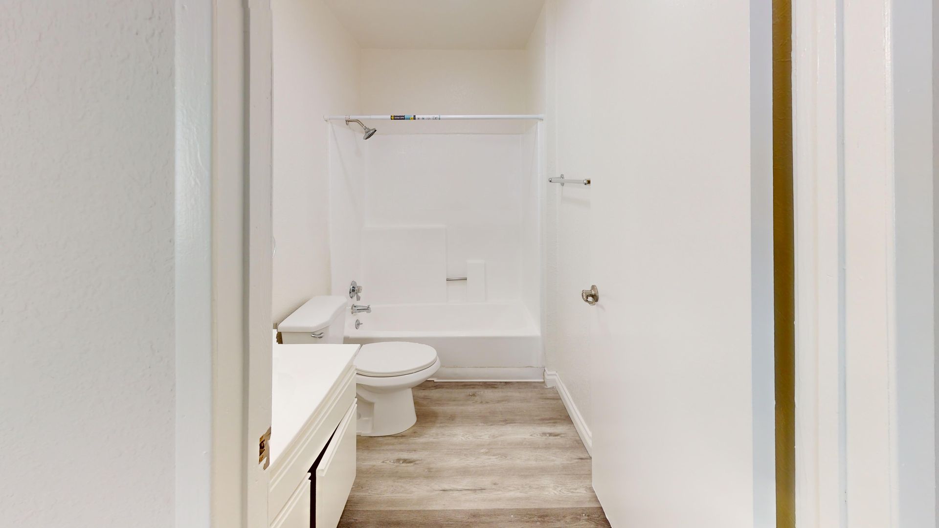 Bathroom with white fixtures, a bathtub/shower, and light-colored wood-look flooring.