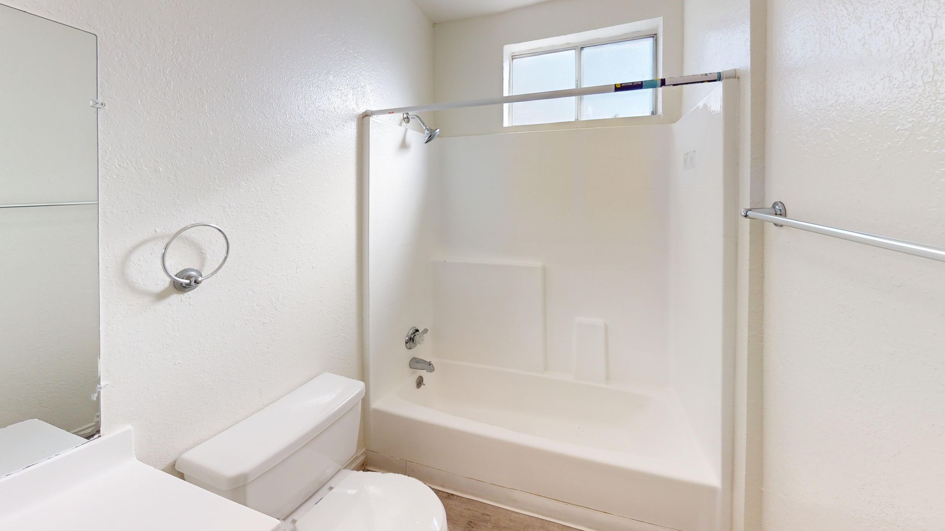 White bathroom with toilet, bathtub, and window.