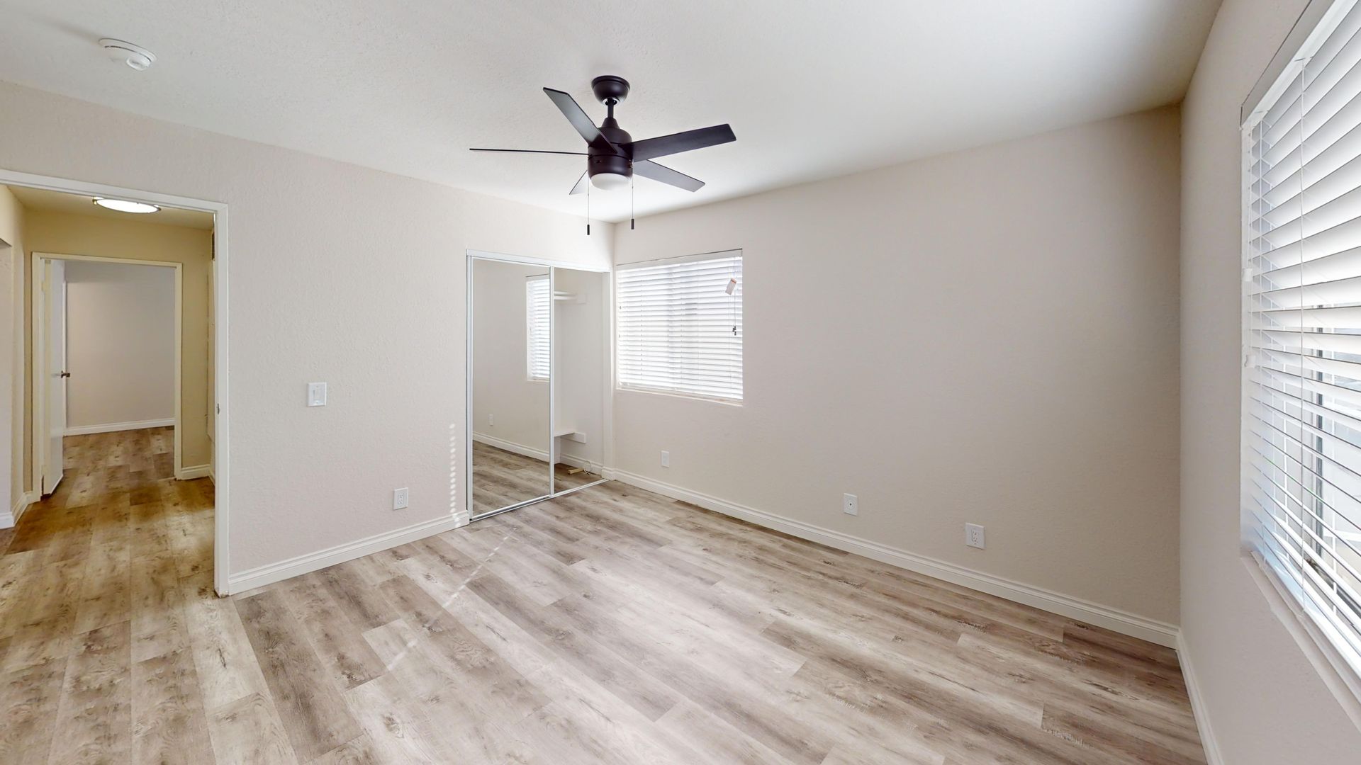 Bedroom with light wood-look floor, large mirror closet, a window, and a ceiling fan.
