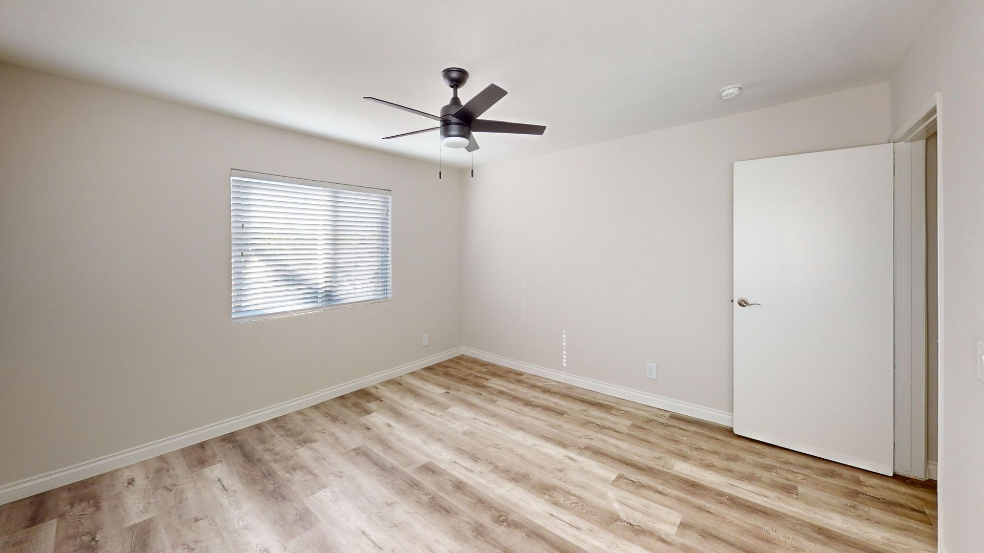 Empty room with light wood floors, a window, a door, and a ceiling fan.
