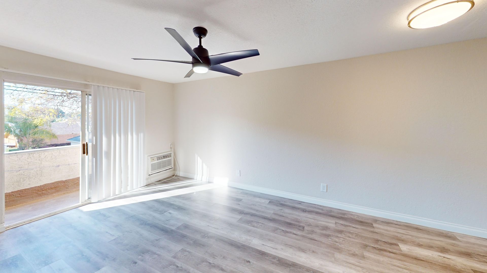 Empty room with sliding glass door, white walls, and wood-look flooring.