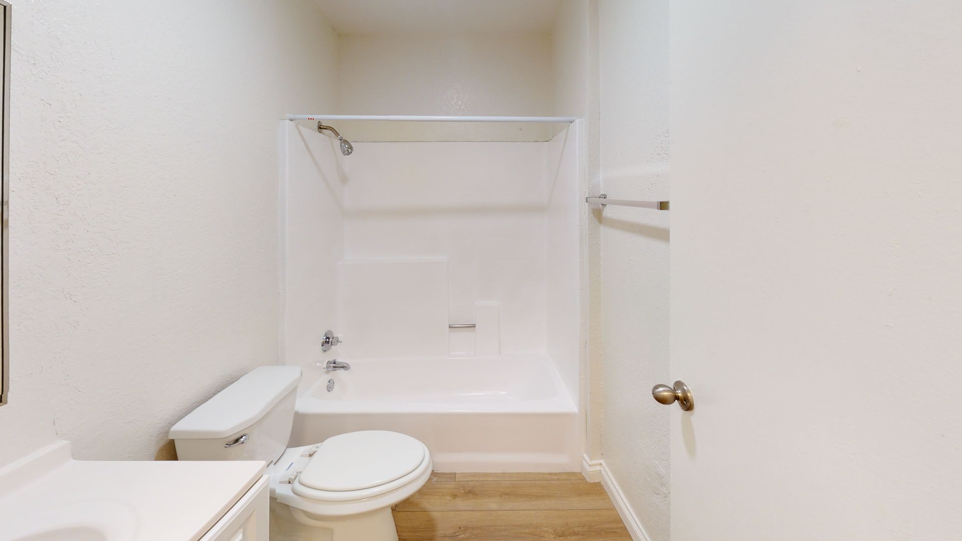 Small, white bathroom with a toilet, shower/tub combo, and a partially open door.