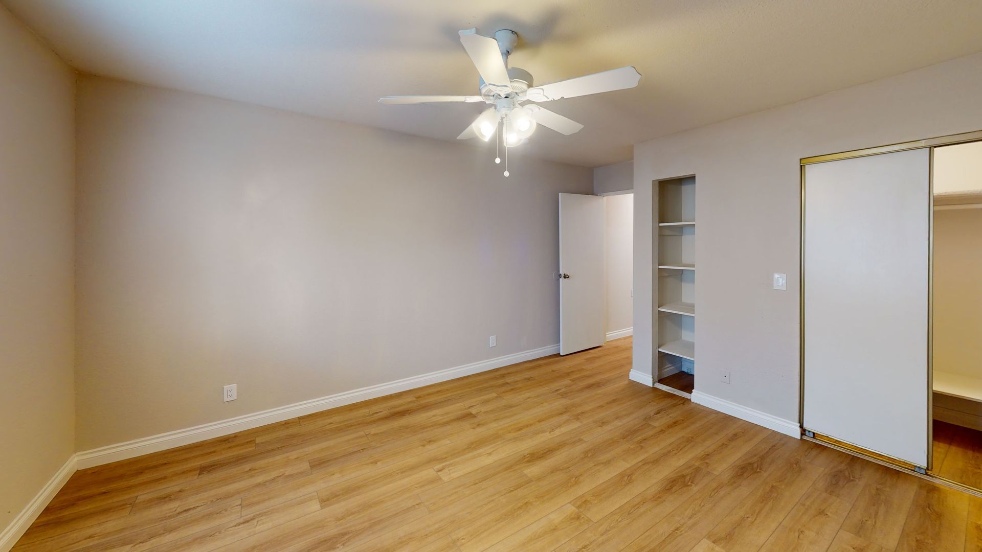 Empty bedroom with wood flooring, ceiling fan, and built-in shelving.