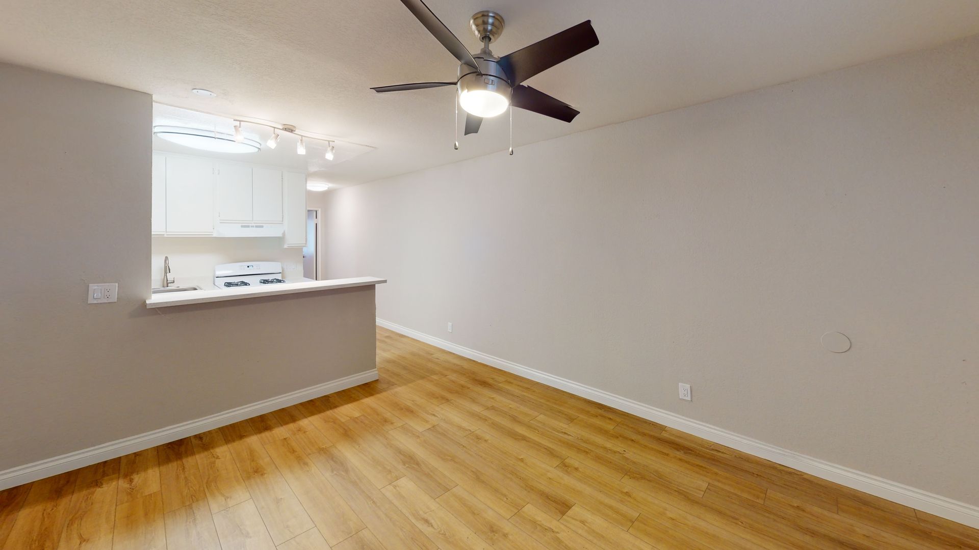 Interior of a room with wooden floors, a kitchen, and a ceiling fan.