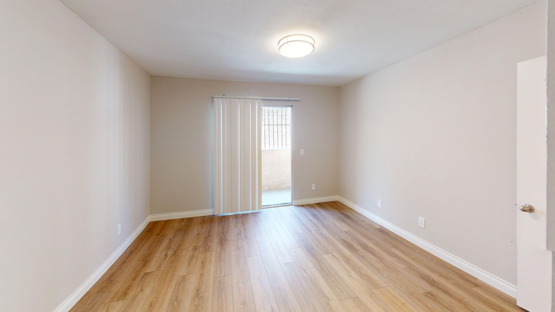 Empty room with wood-look floor, balcony access, and light beige walls.