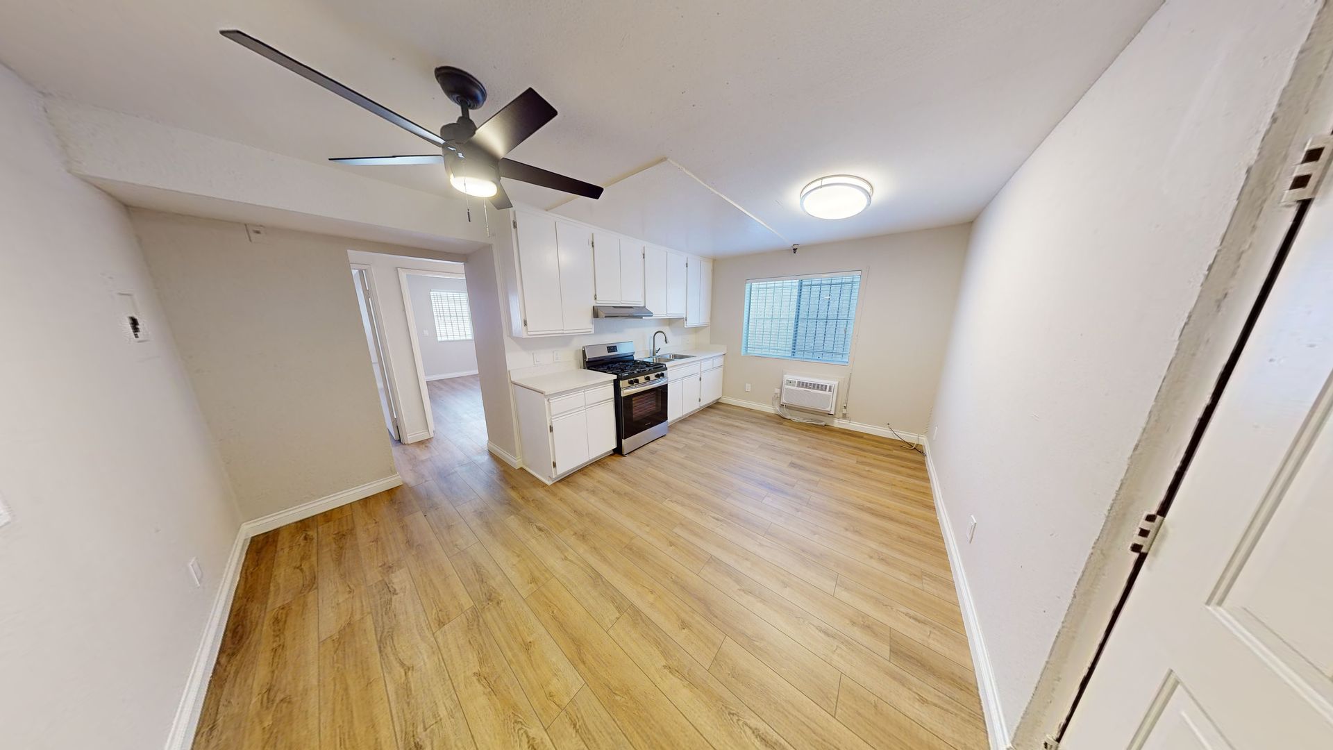 Interior of an apartment: kitchen area with white cabinets and a living space with wood-look flooring.
