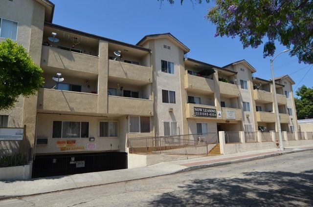 Three-story beige apartment building with balconies and a ramp; sunny day.