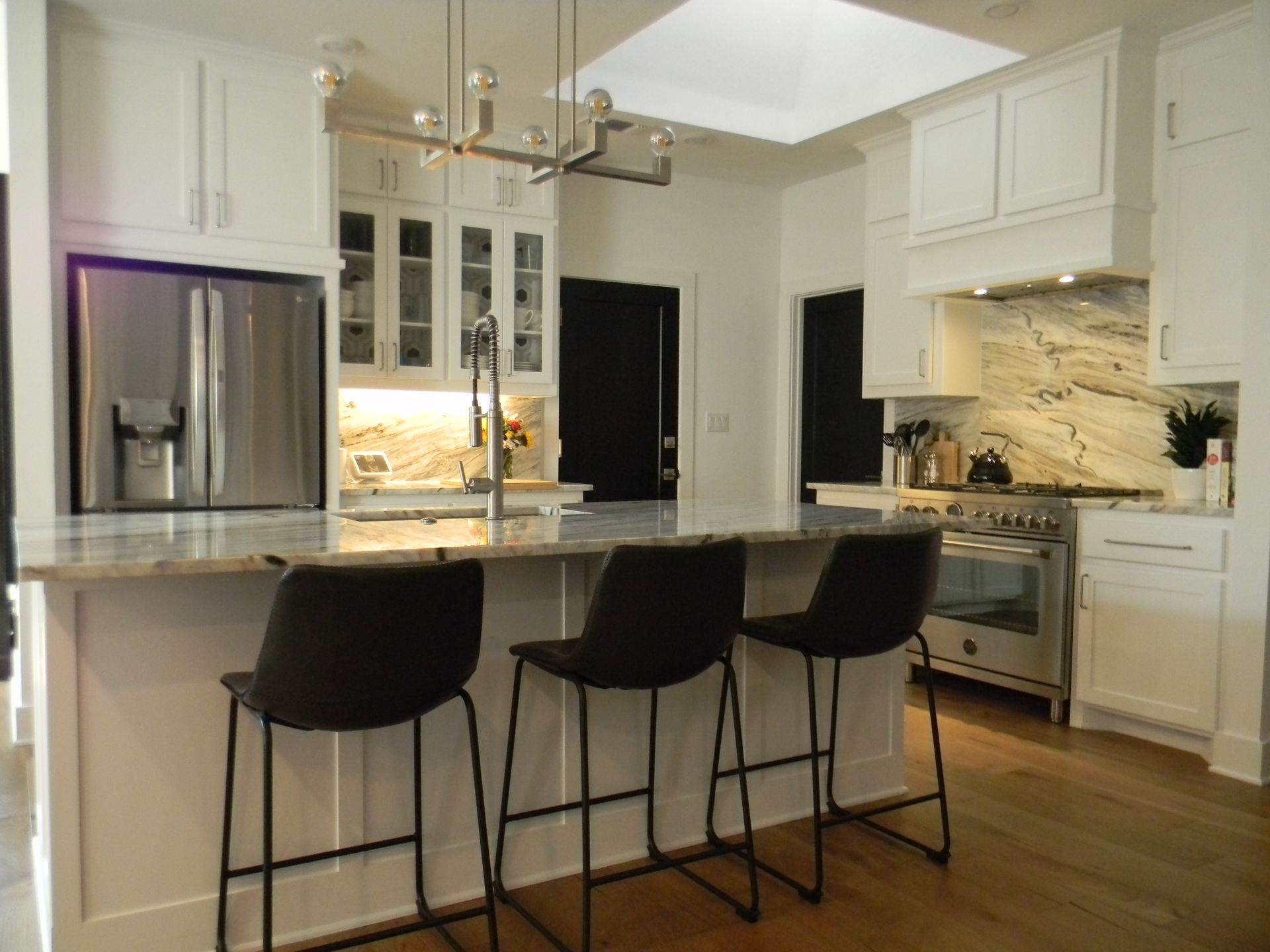 A kitchen with white cabinets and black stools and a large island.