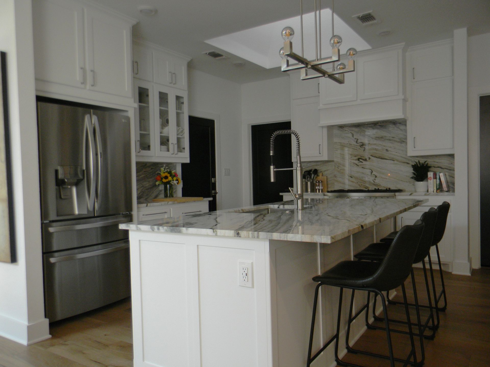 A kitchen with white cabinets , stainless steel appliances , marble counter tops and a large island.
