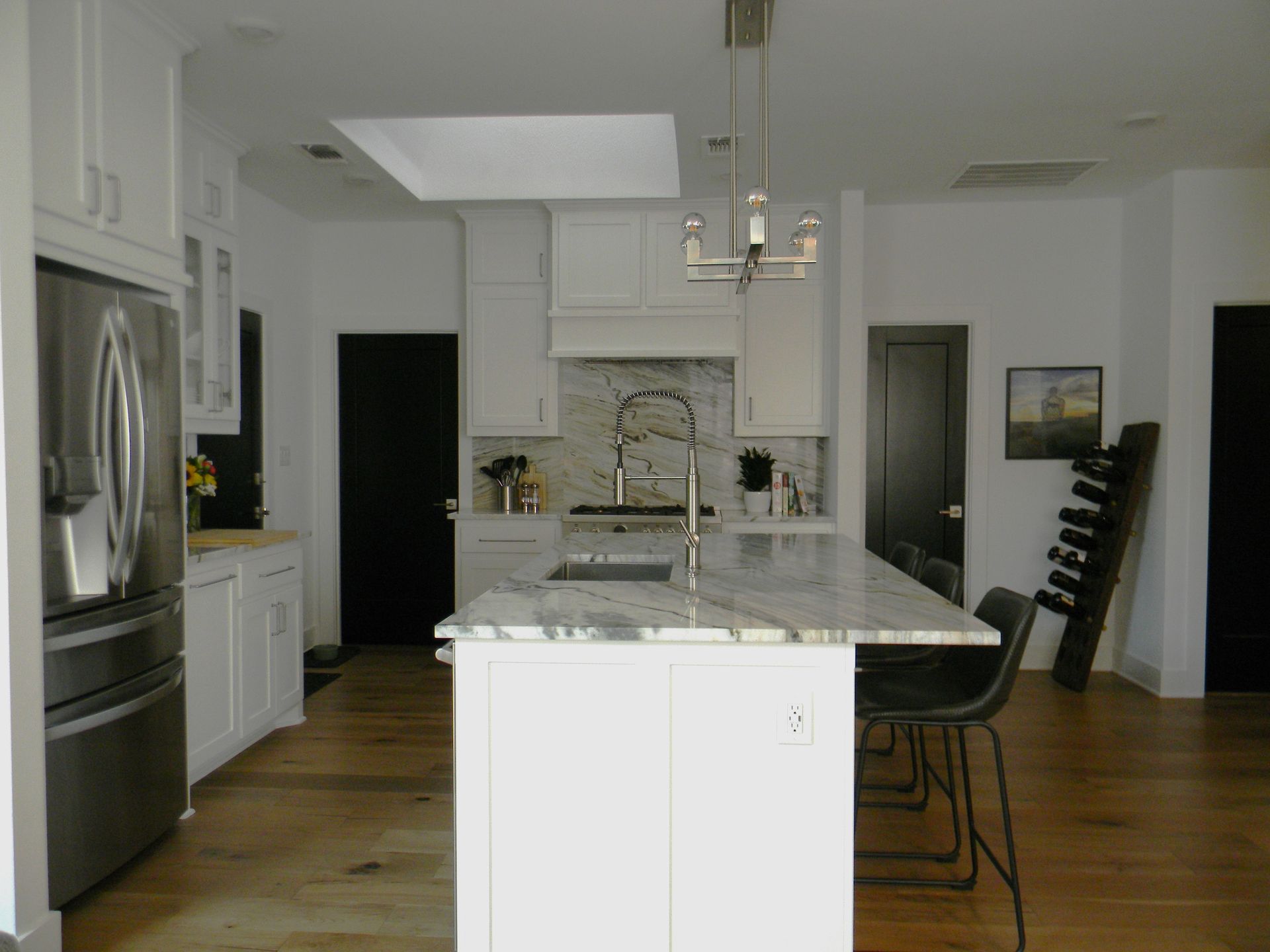 A kitchen with white cabinets and stainless steel appliances and a large island in the middle.