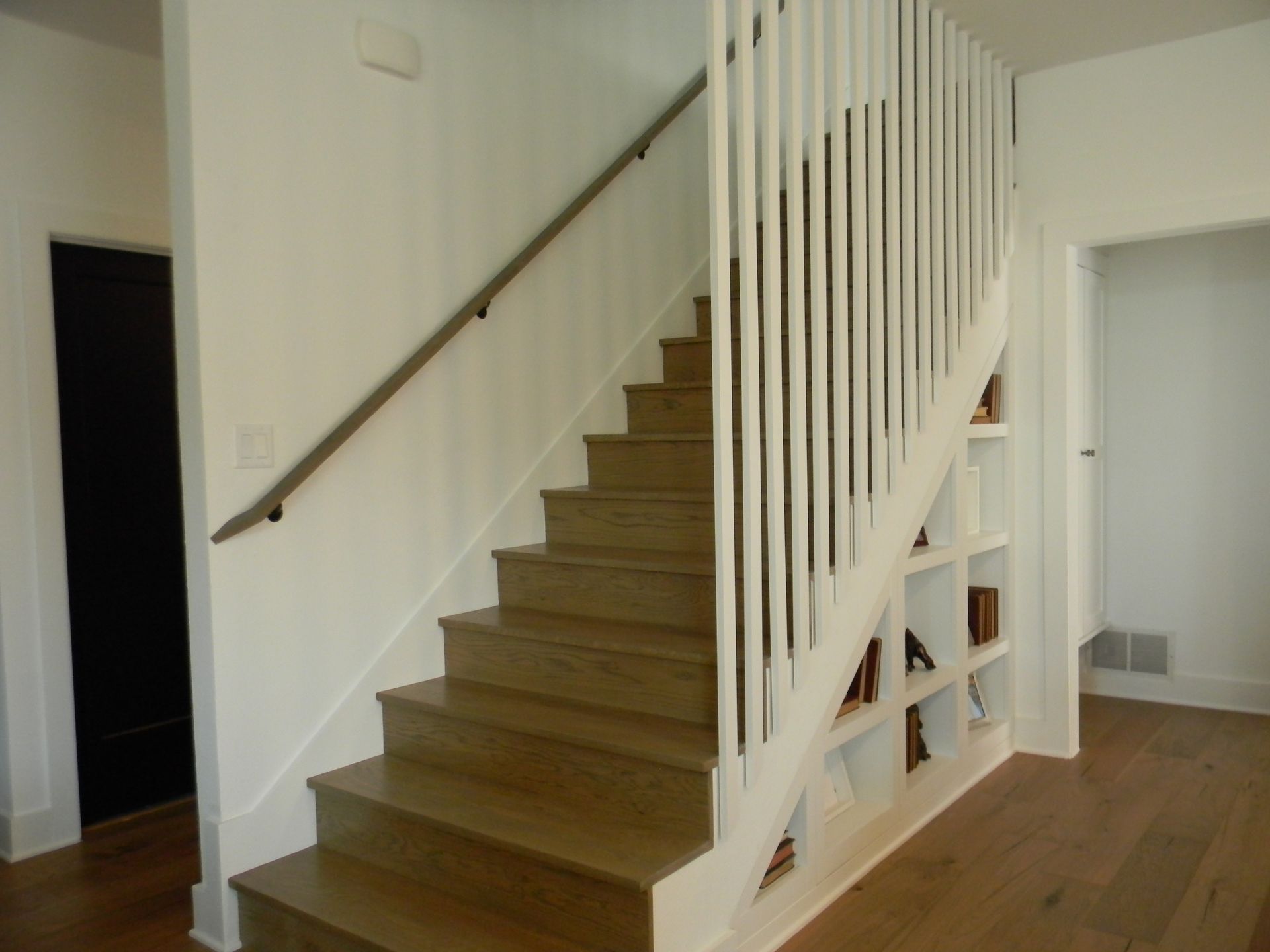 A wooden staircase with a white railing and shelves underneath