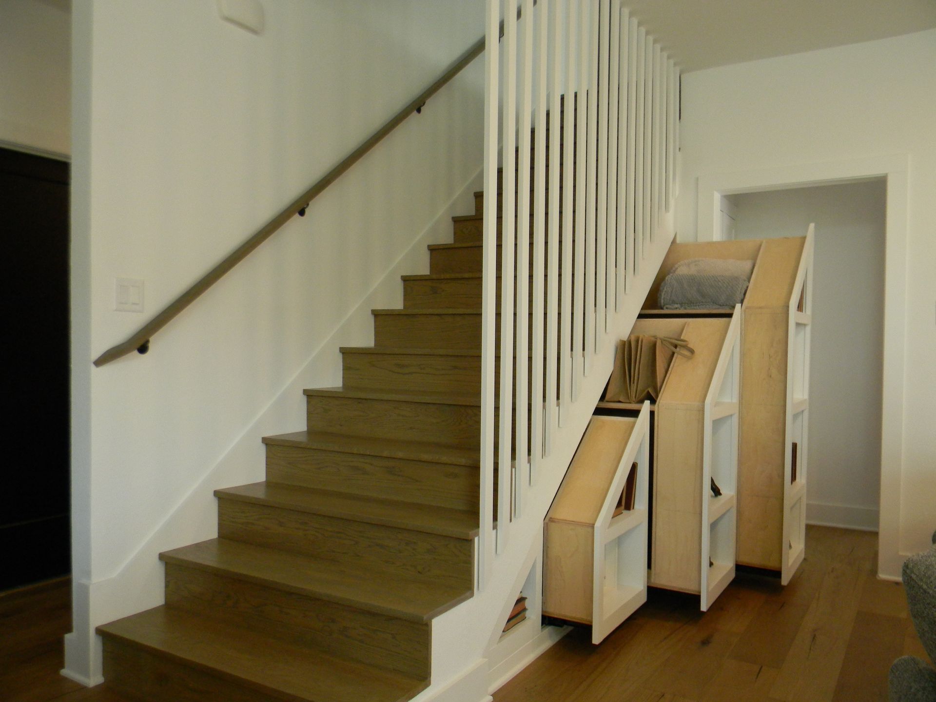 A wooden staircase with a white railing and drawers underneath
