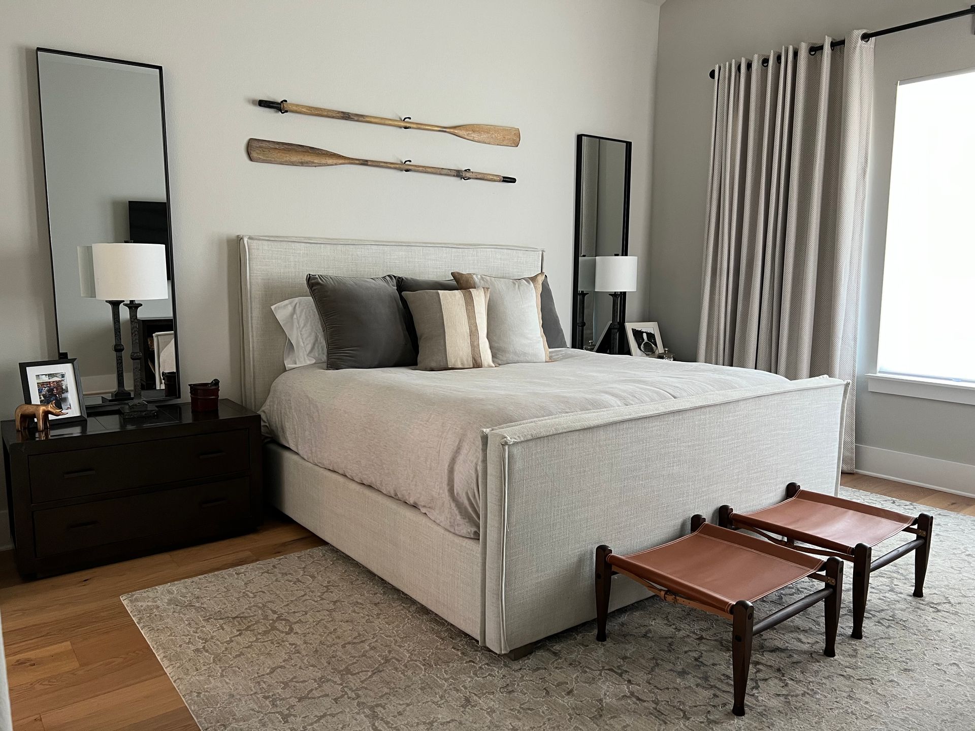 A bedroom with a large bed , two benches , two mirrors and a window.