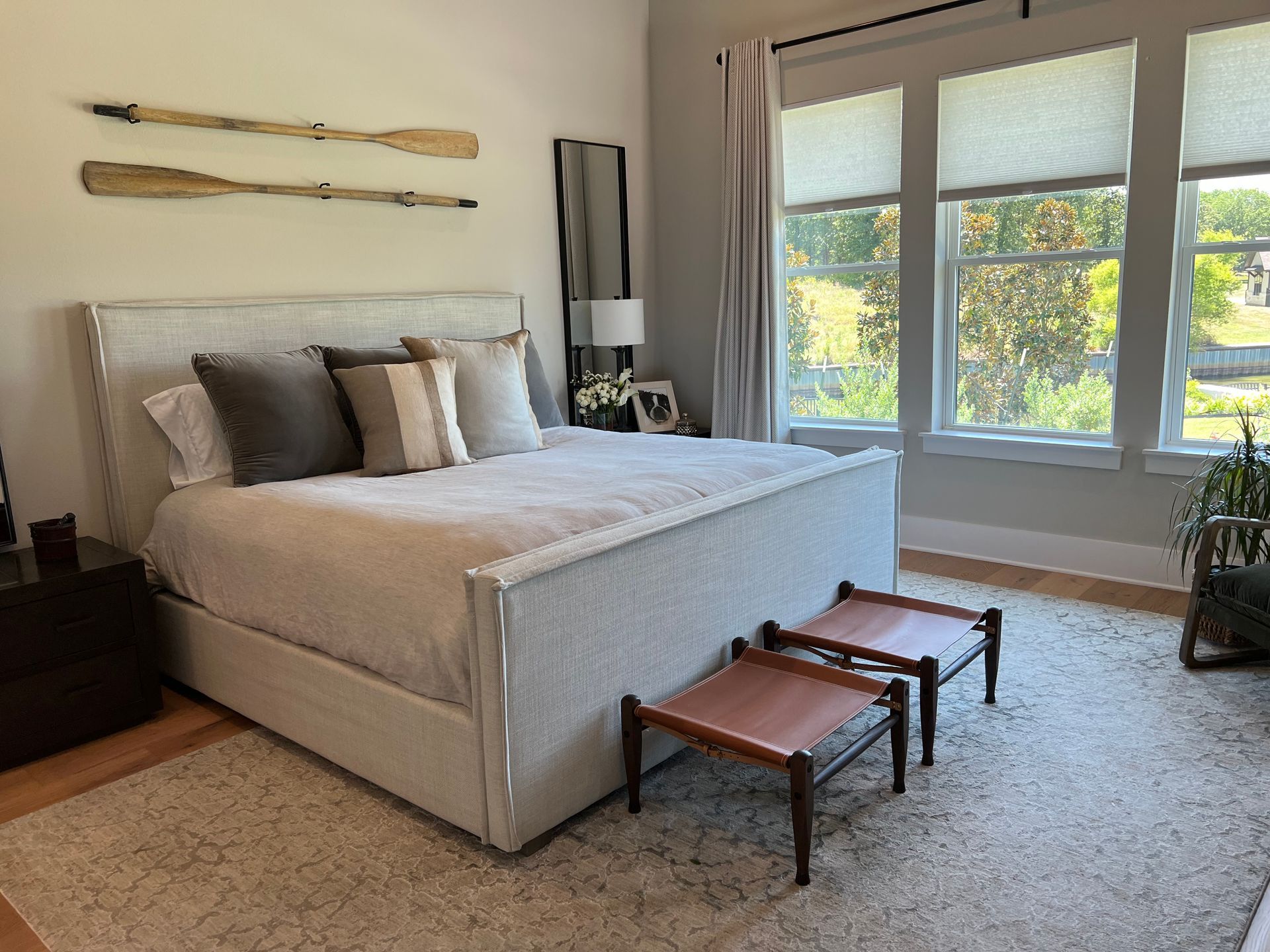 A bedroom with a large bed , two ottomans and two windows.