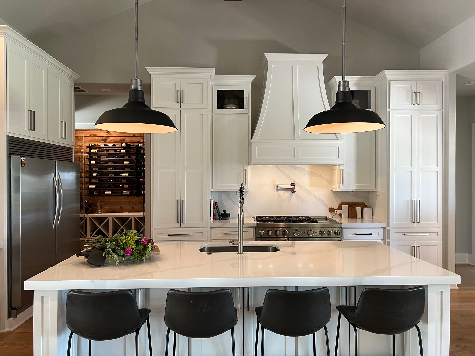A kitchen with white cabinets and black chairs and a large island.