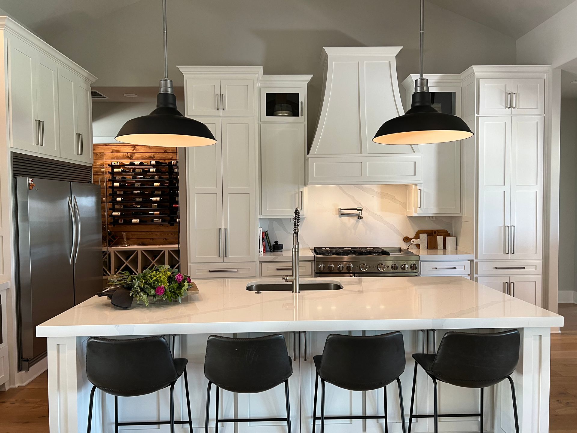 A kitchen with white cabinets and black stools and a large island.