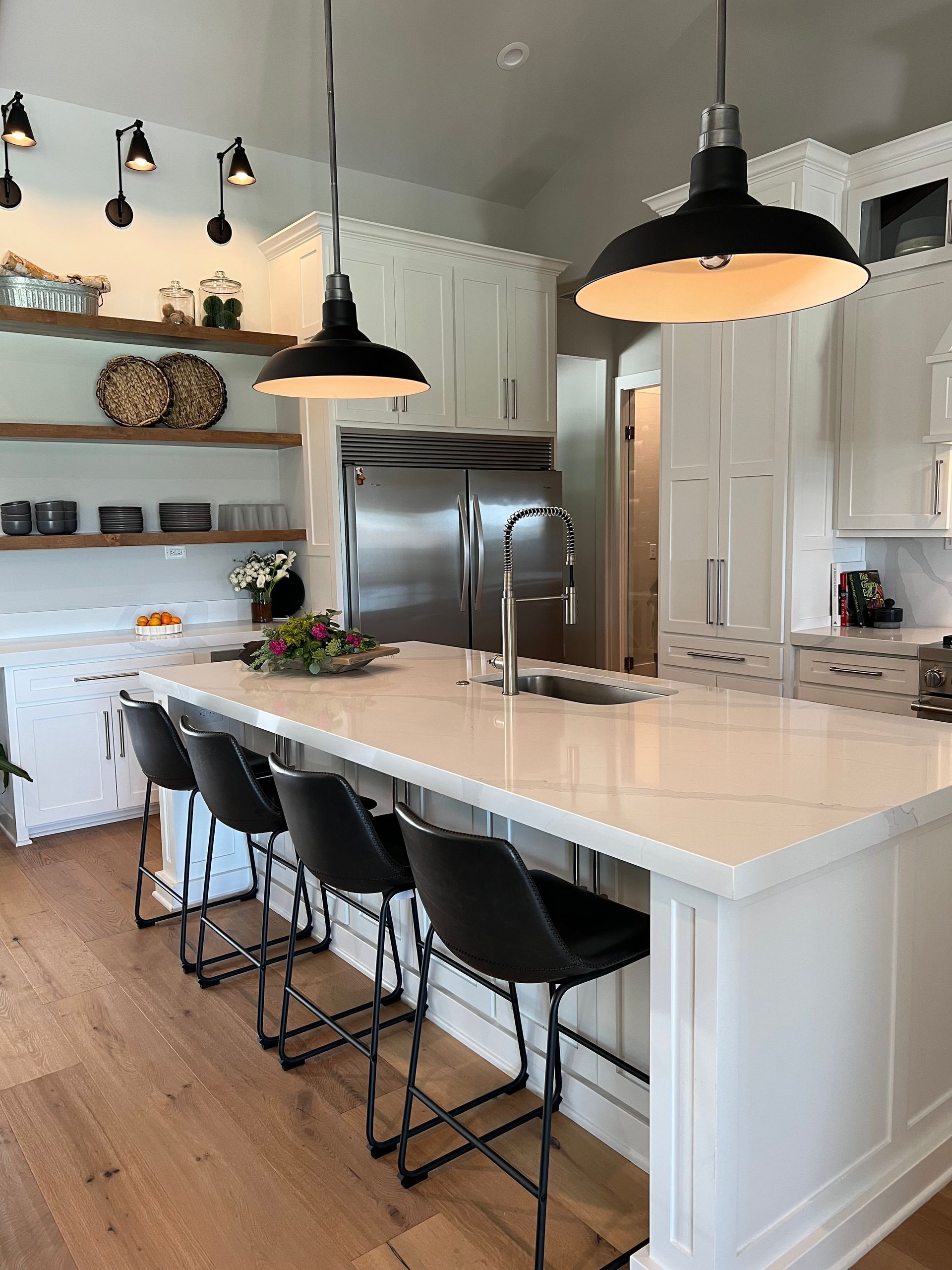 A kitchen with white cabinets , stainless steel appliances , a large island , and black chairs.