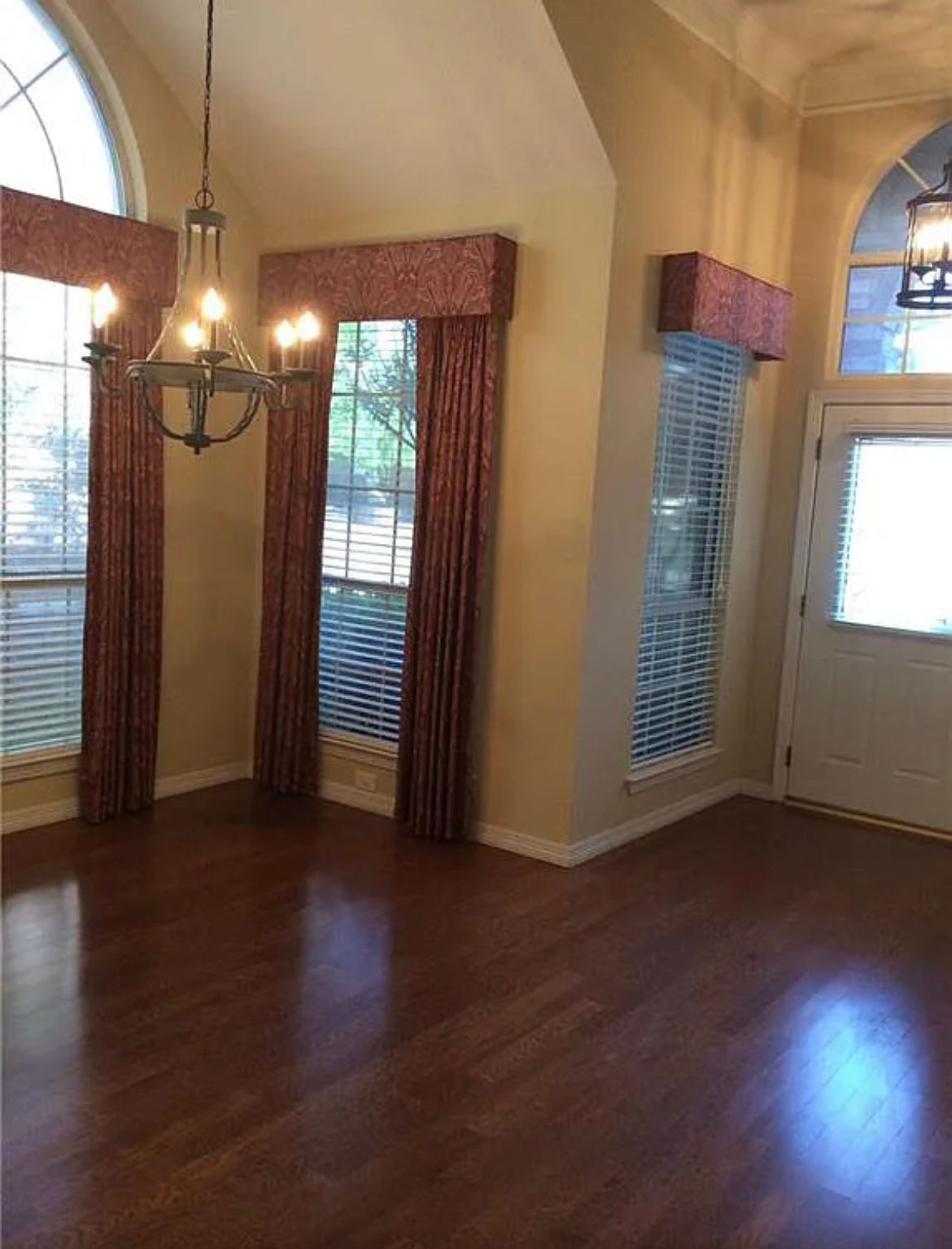 An empty living room with hardwood floors and a chandelier hanging from the ceiling.