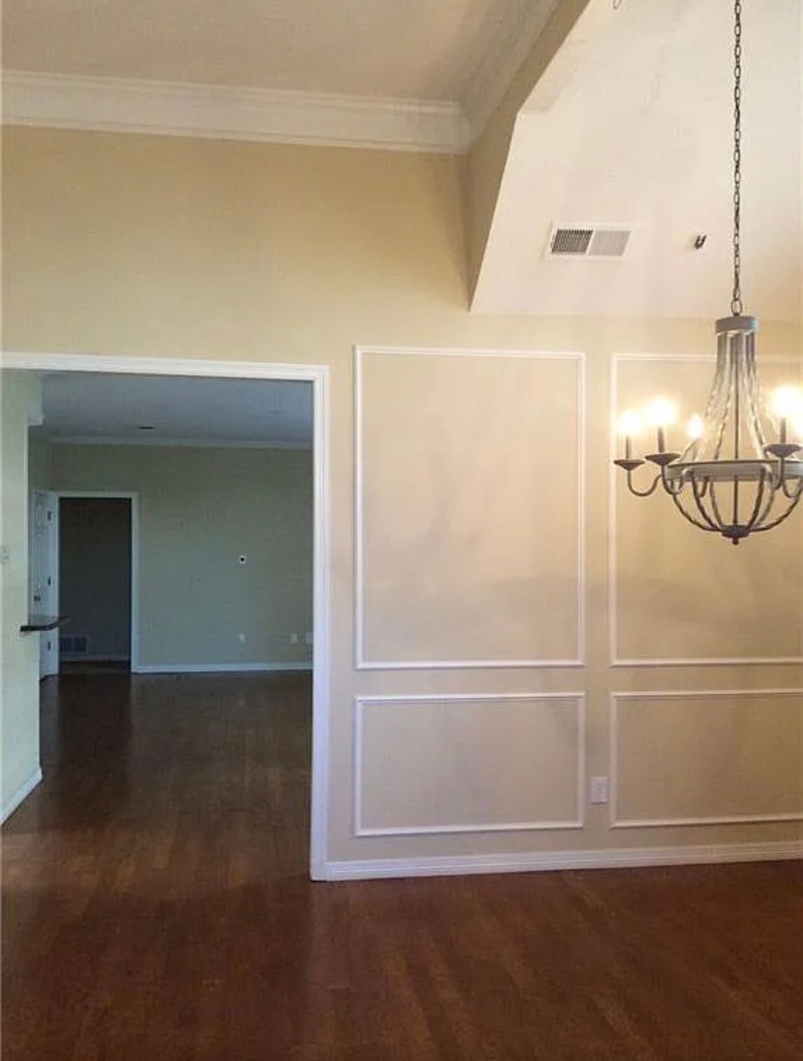 An empty dining room with a chandelier hanging from the ceiling.