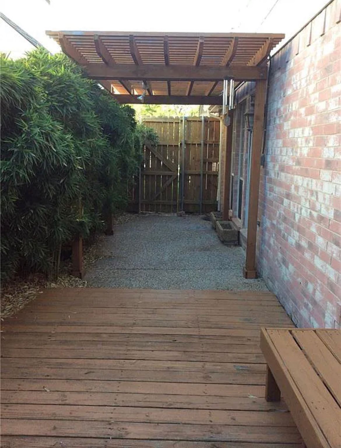 A wooden deck with a bench under a pergola