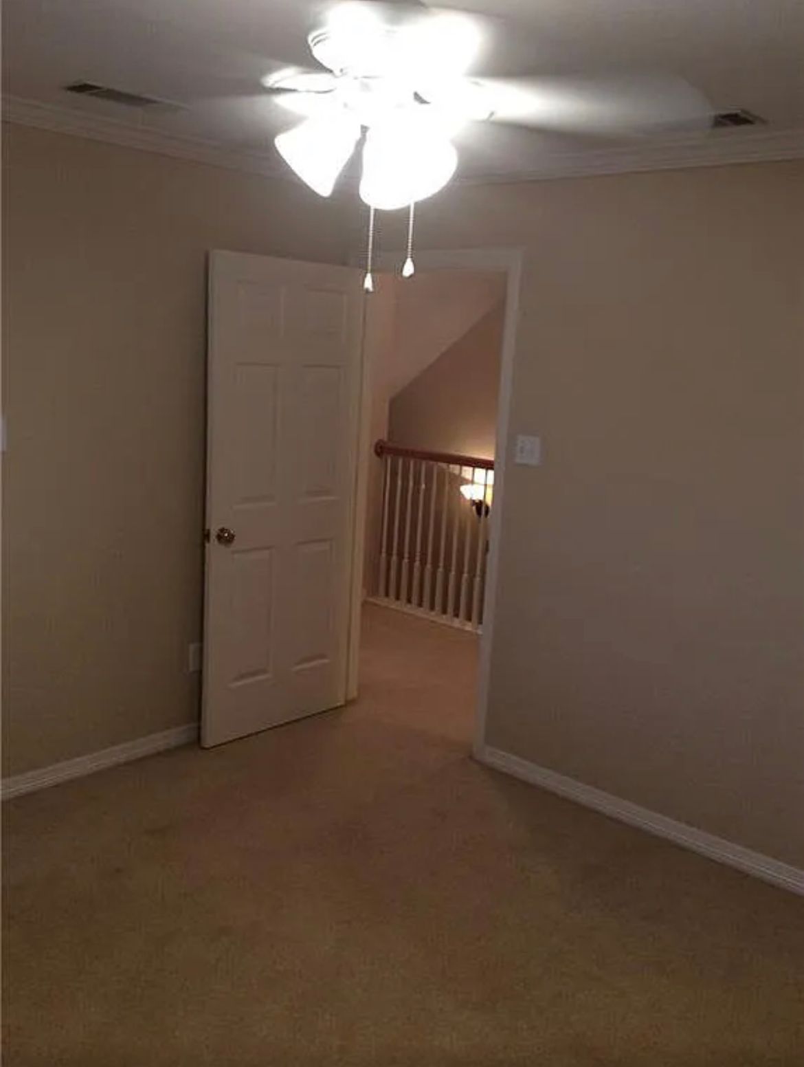 An empty bedroom with a ceiling fan and a door leading to a balcony.