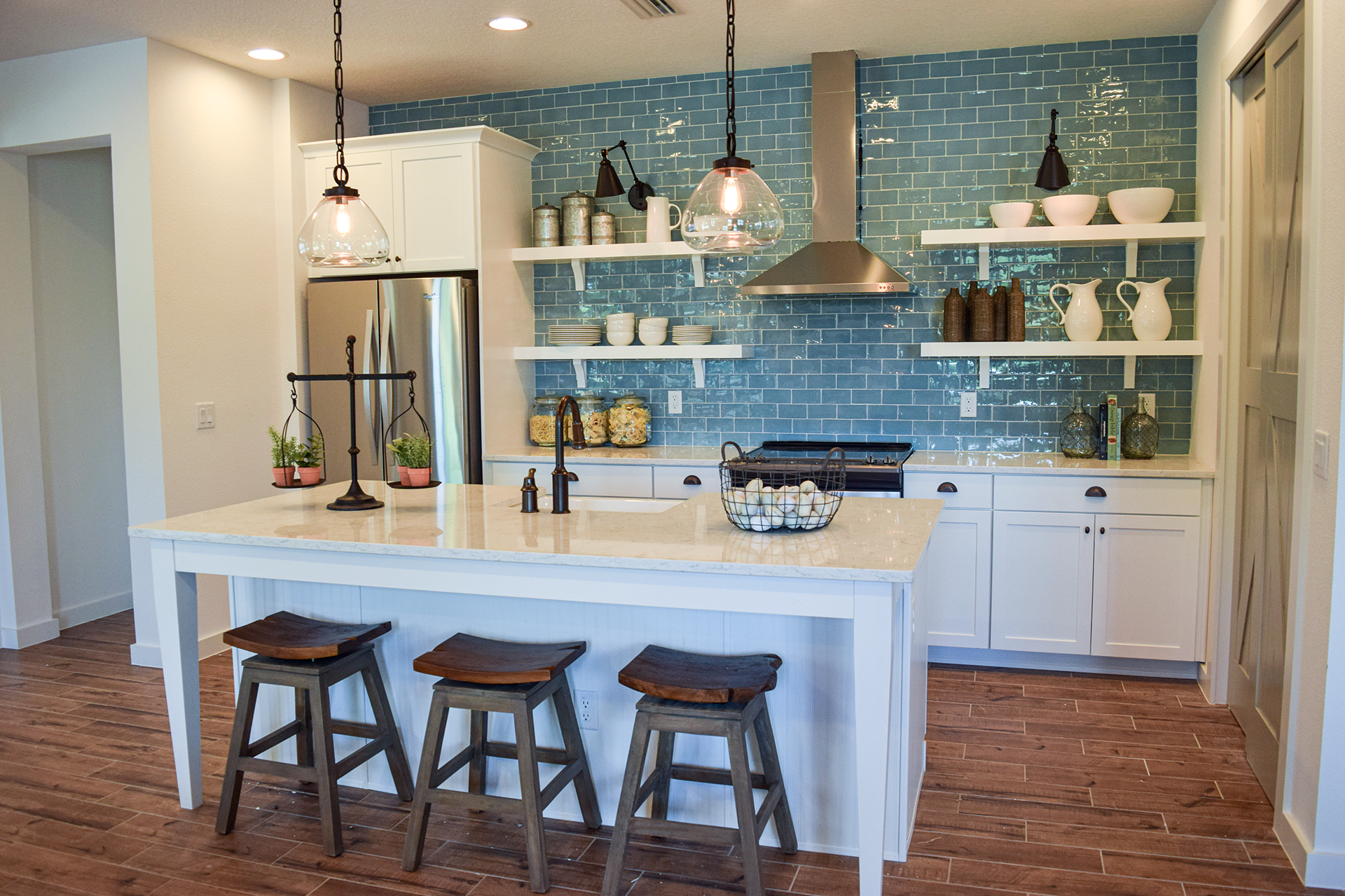 A kitchen with a large island , stools , a refrigerator and a stove.