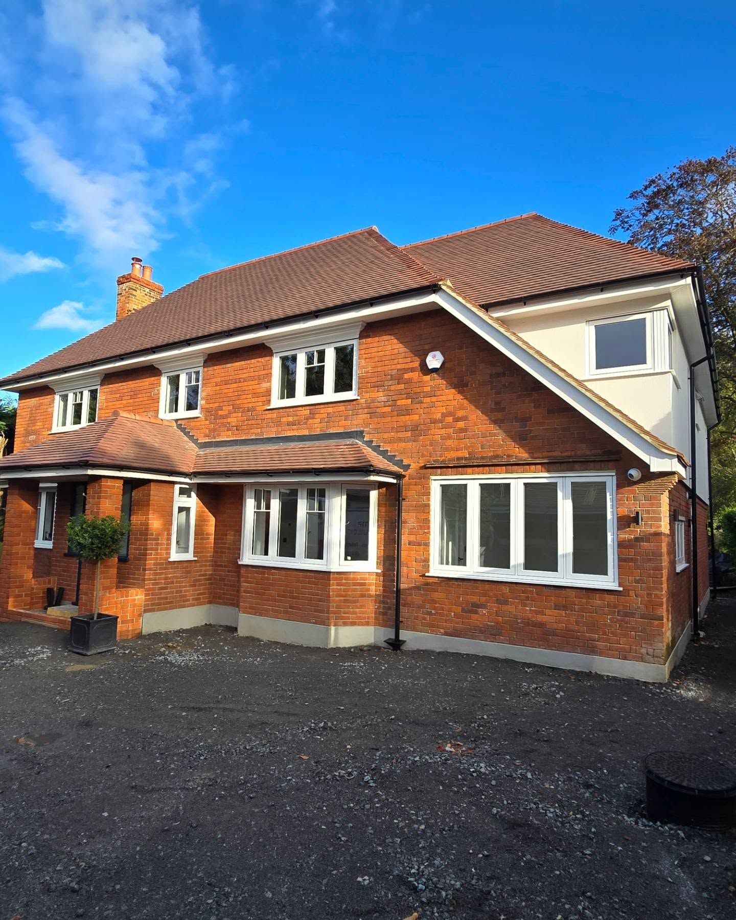 Two-story brick house with white trim windows and brown roof, against a bright blue sky.