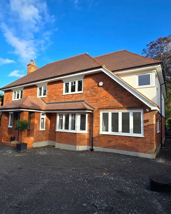 Two-story brick house with white trim windows and brown roof, against a bright blue sky.