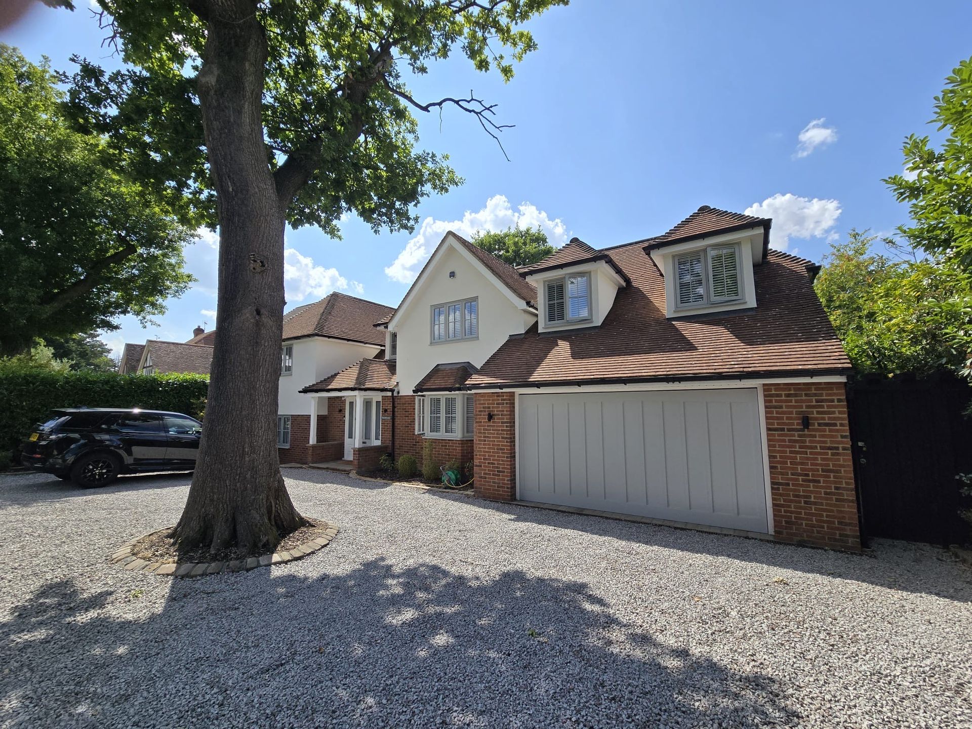 A two-story house with a gravel driveway, garage, and a large tree in front.