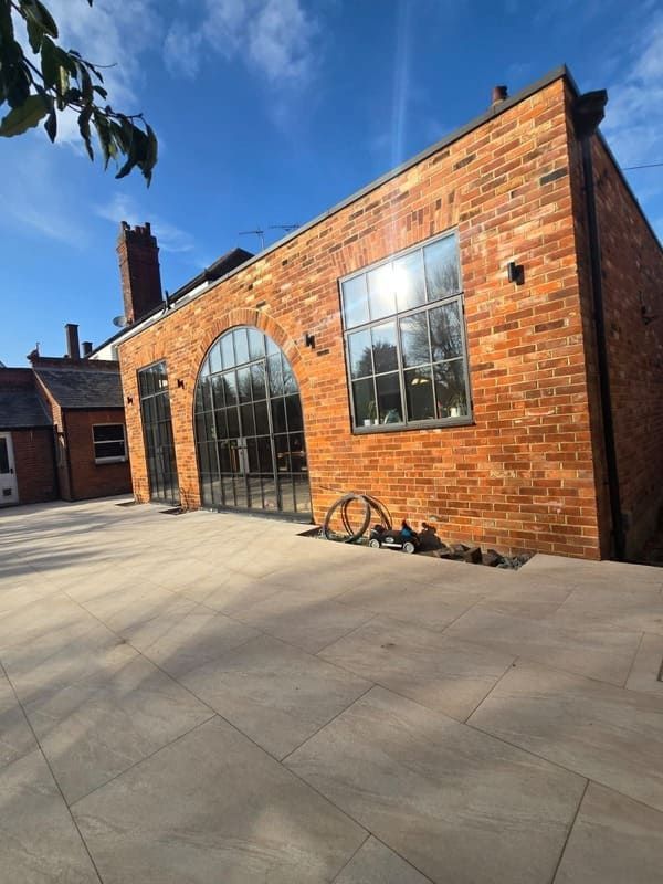 Red brick building with large metal-framed windows, against a blue sky, on a paved patio.